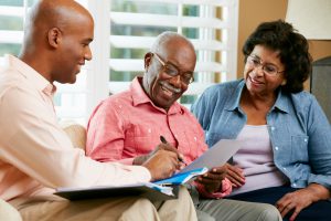 Financial Advisor Talking To Senior Couple At Home Signing Documents Smiling